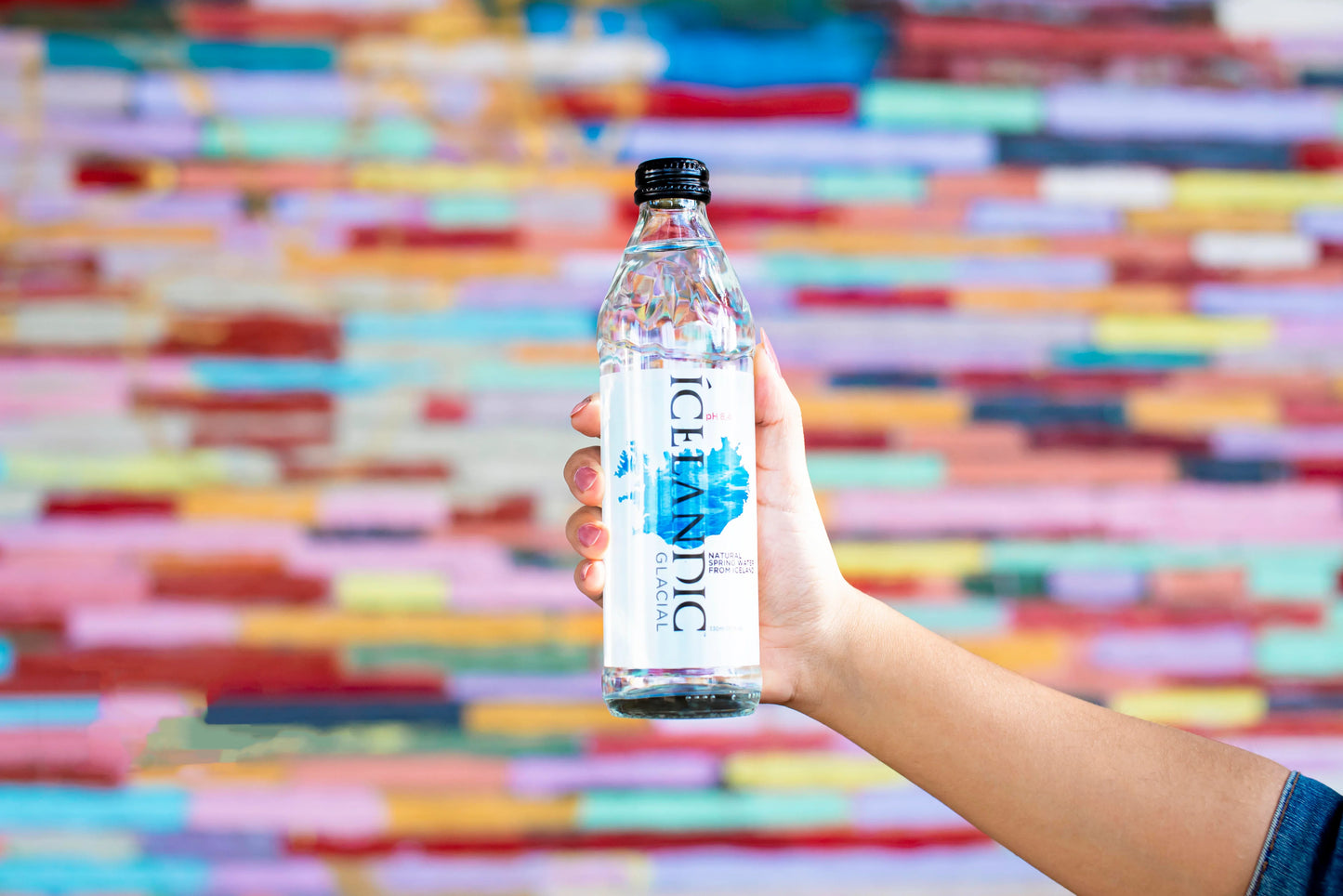 Hand holding Icelandic Glacial water bottle against colorful blurred background