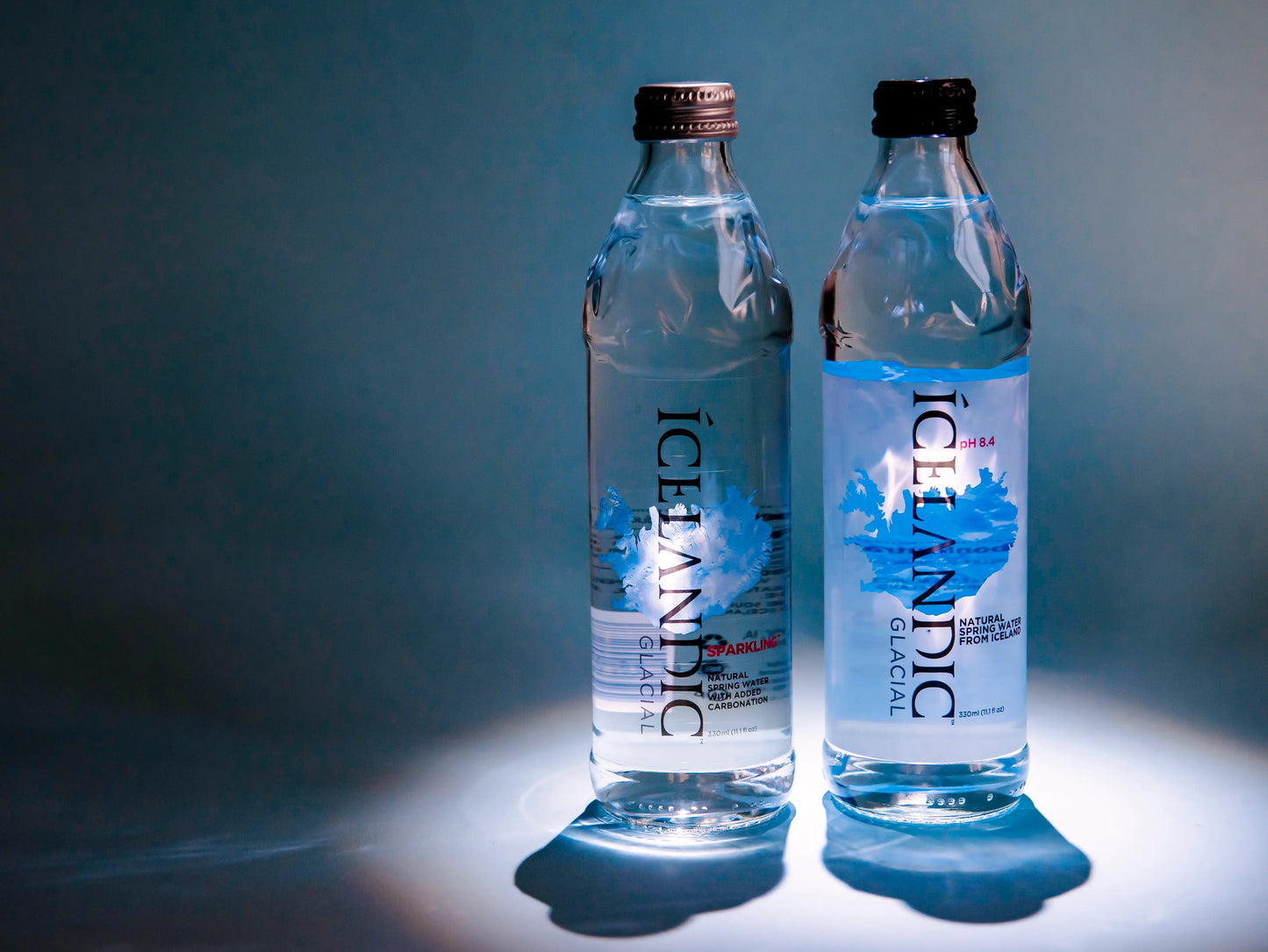 Two Icelandic Glacial natural spring water bottles with blue label on a light background
