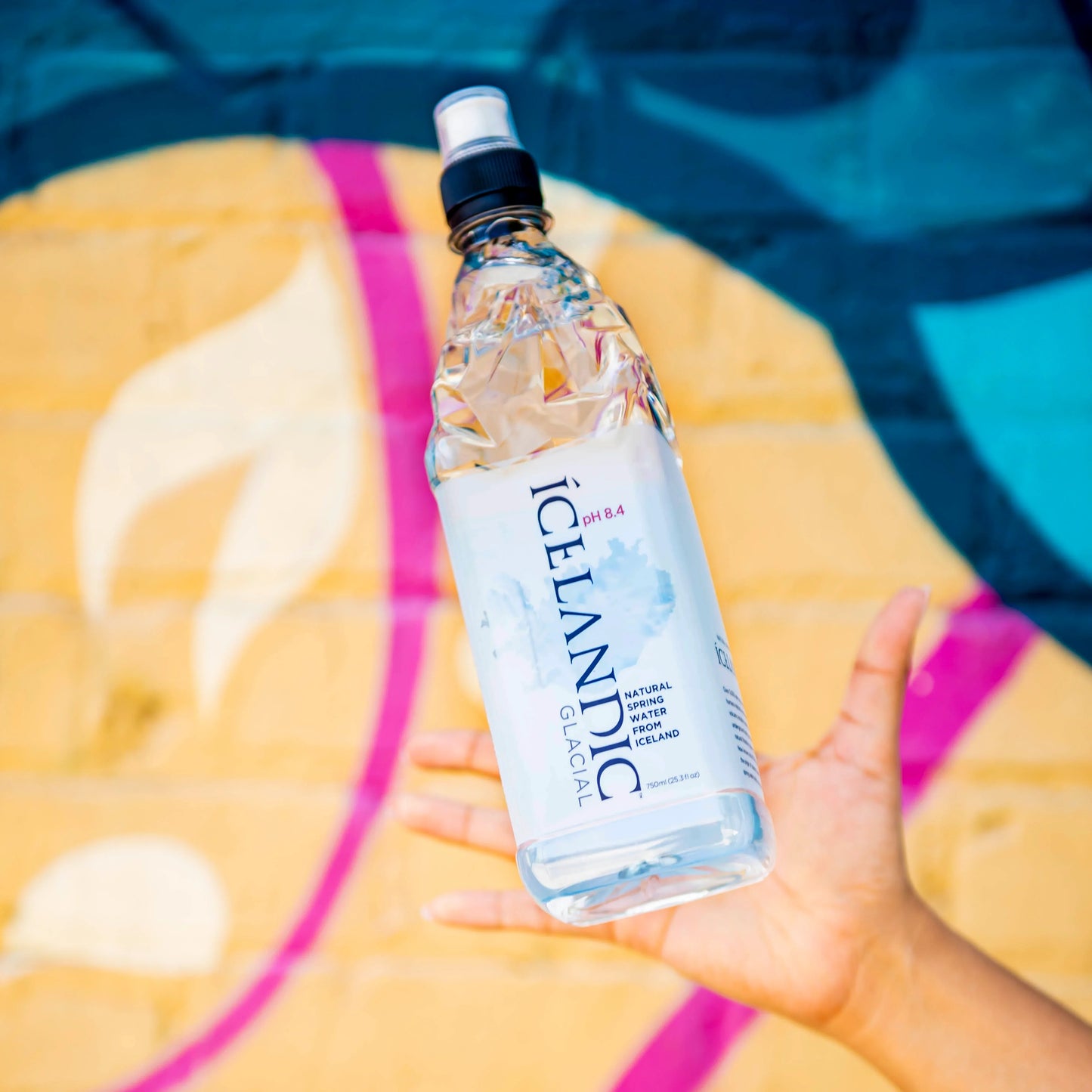 Hand holding Icelandic natural spring water bottle against colorful mural background
