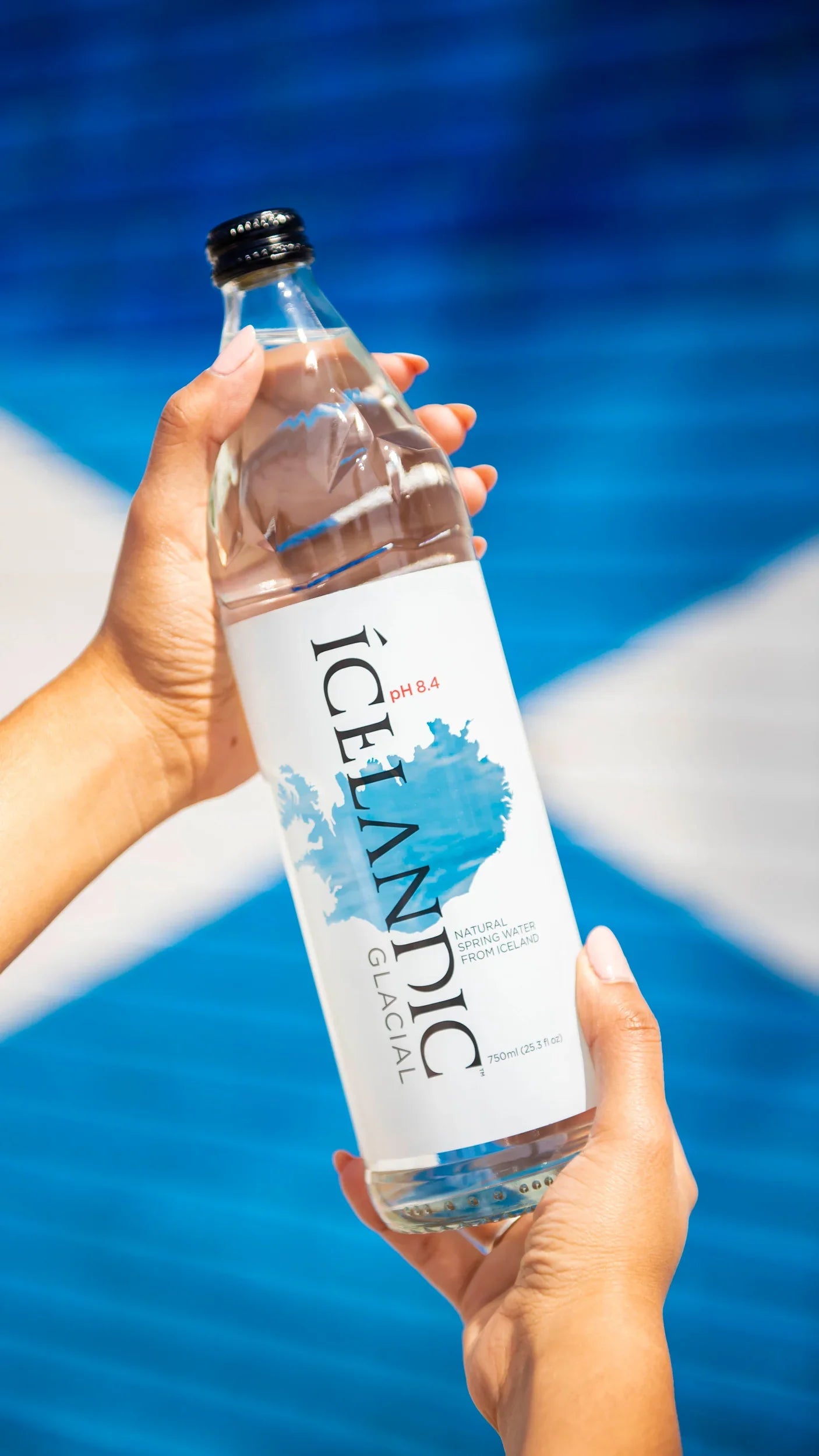Hand holding a clear glass bottle of natural spring water with blue and white label