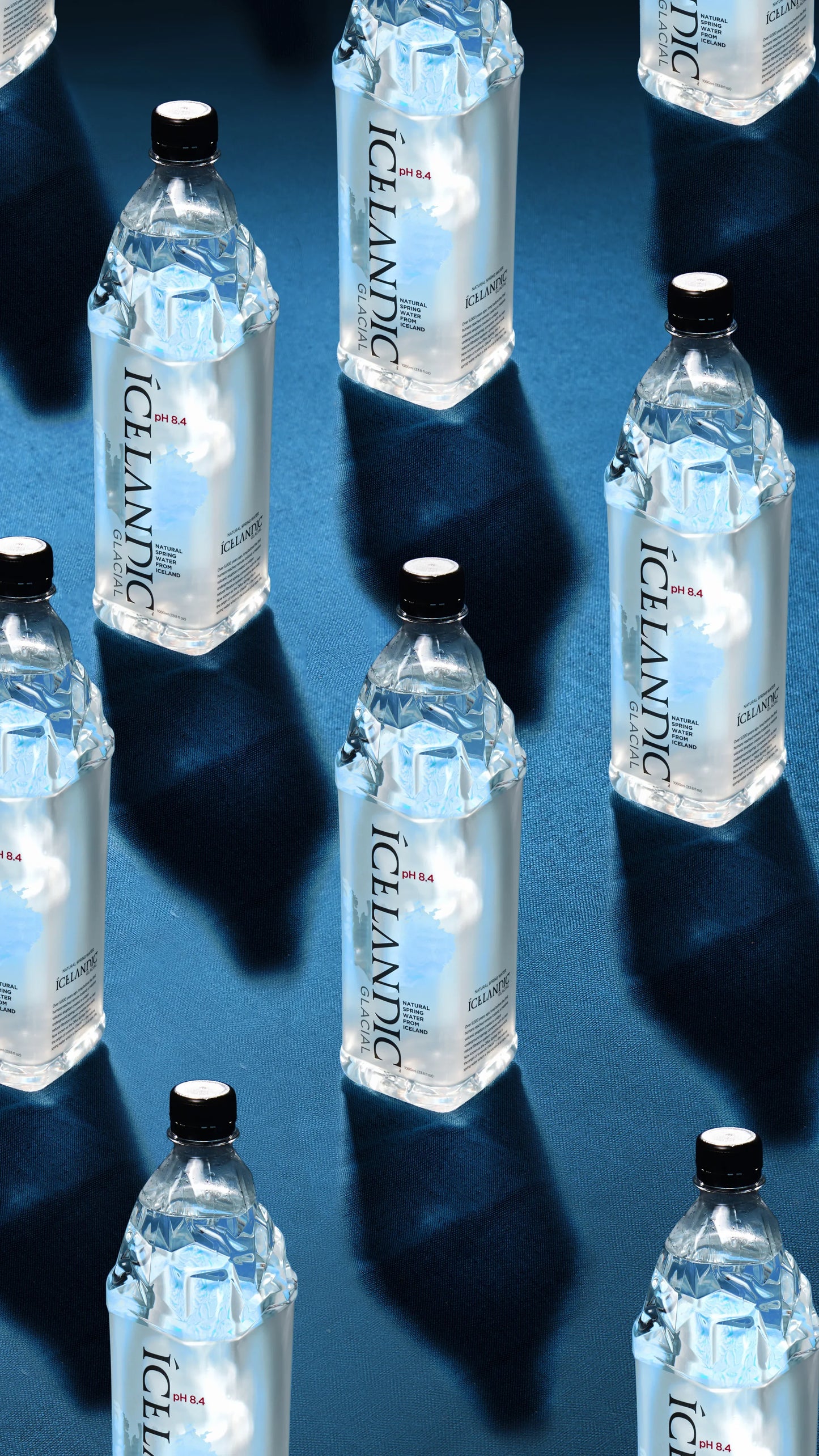 Multiple Icelandic Glacial water bottles with clear labels on a blue textured surface